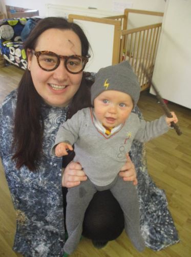 A baby dressed up as Harry Potter sitting on the lap of a nursery worker also dressed up as Harry Potter