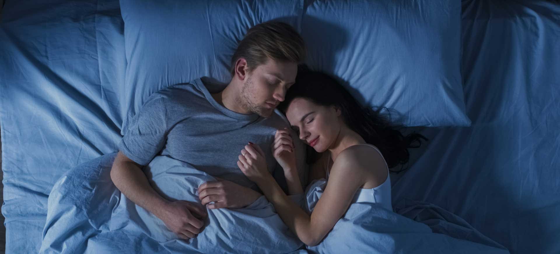 A top-down view of a couple sleeping in bed in a dark bedroom
