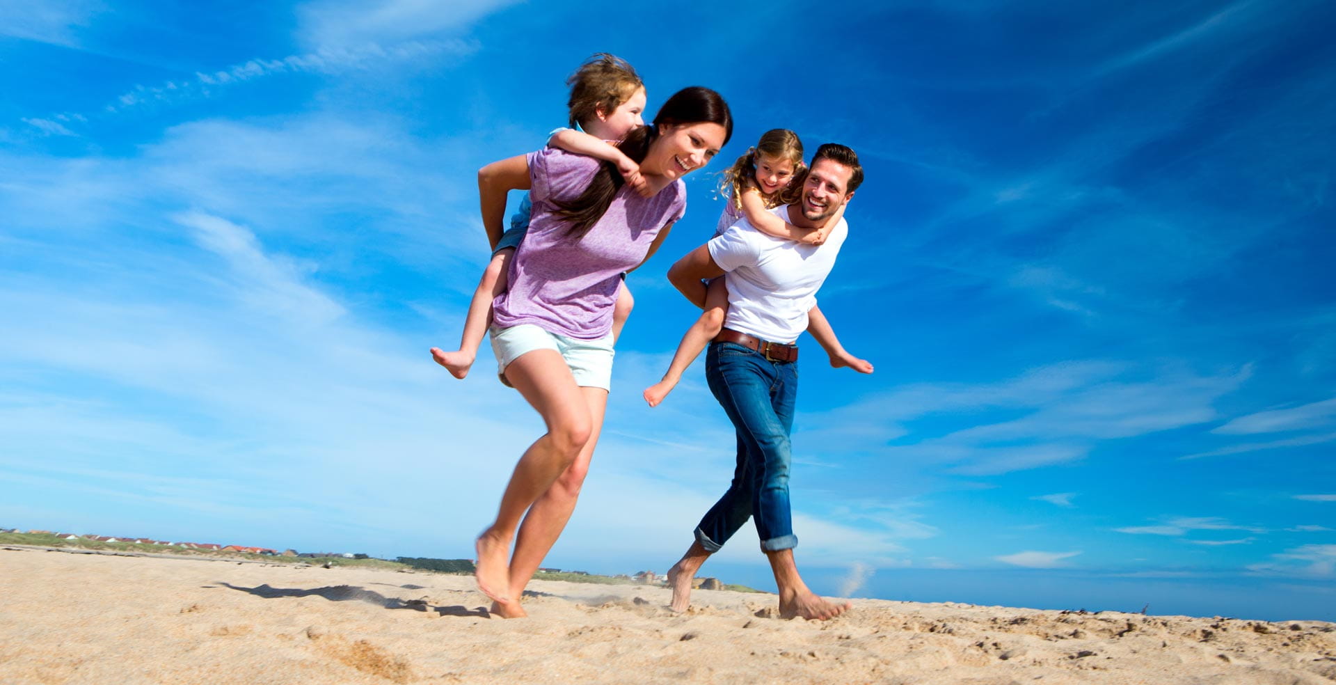 Parents giving their kids piggy backs across the beach