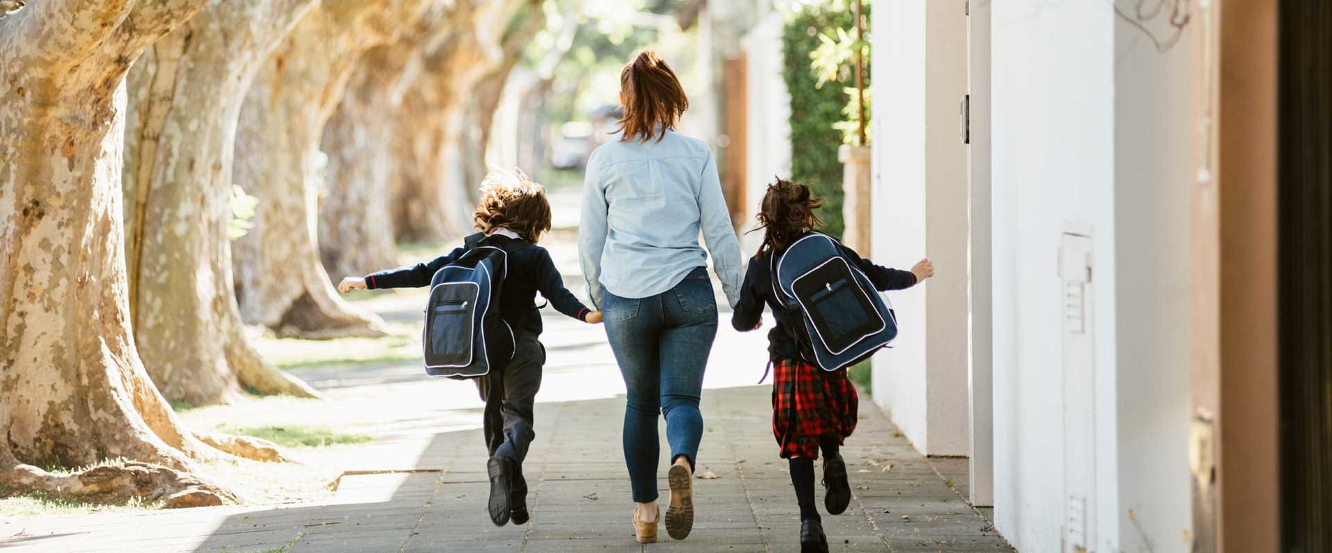 A mother holds hands with her two children as they run away to school